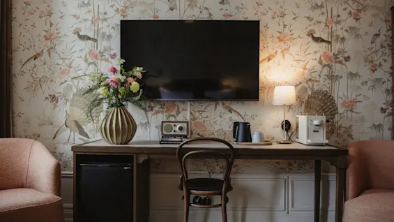 Home Hotel Baltzar - Deluxe Double. A stylish hotel room featuring a desk with a TV, coffee maker, and elegant floral wallpaper.