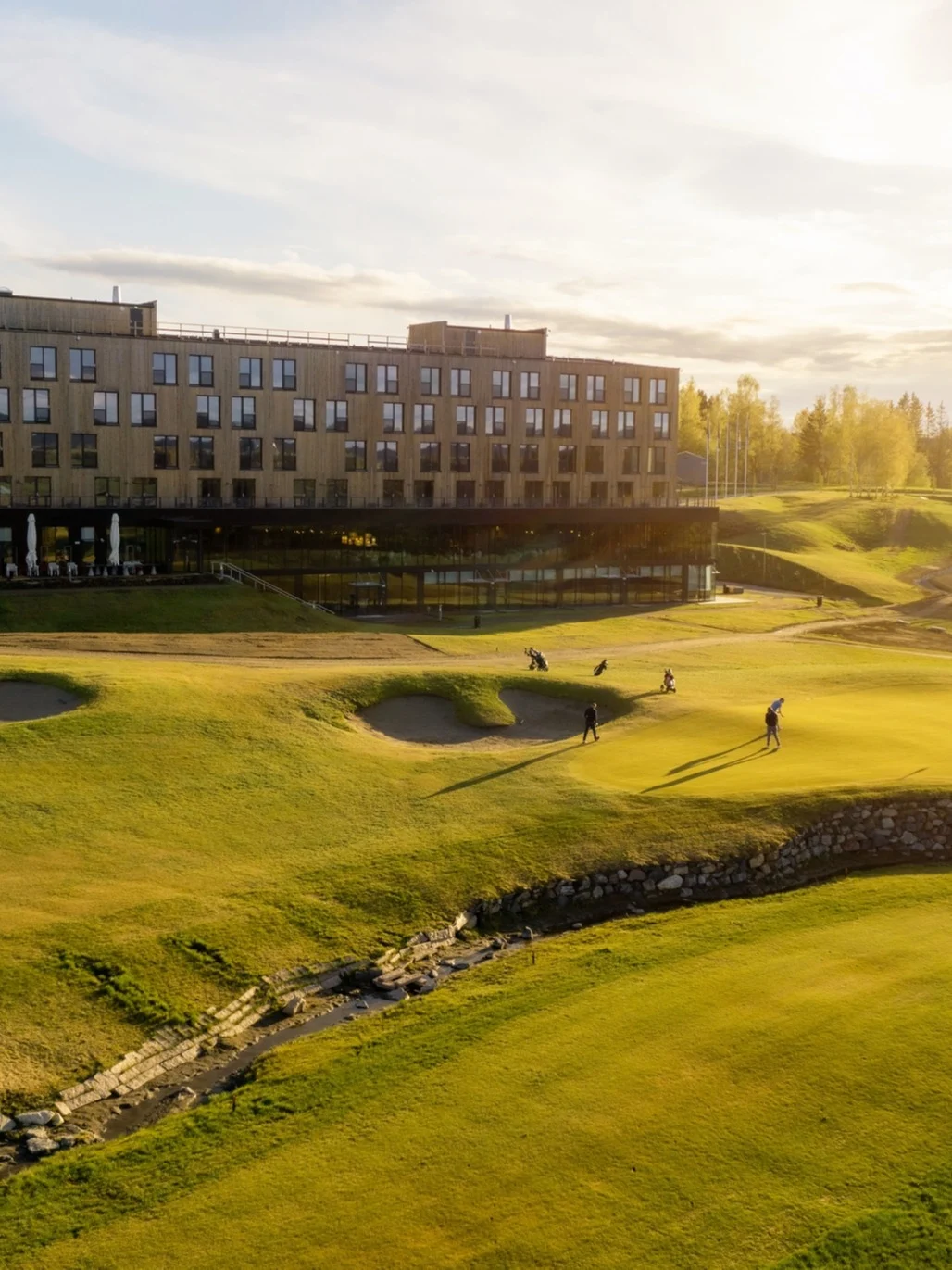 Golfers play on a course near a modern building bathed in sunset light.