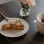 A delightful moment with a slice of cake and a warm cup of tea, accompanied by fresh flowers on a dark table.