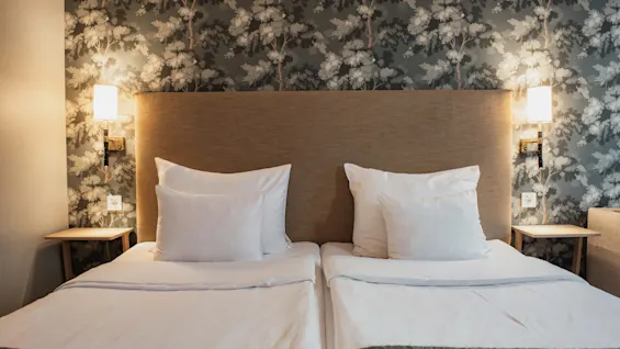 Home Hotel Wellington. Et hyggeligt hotelværelse med to senge, en blød sengegavl og elegant tapet med træmønster.