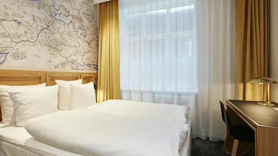 Et hyggeligt hotelværelse med en komfortabel seng, et skrivebord til arbejde eller studier og et vindue med gardiner.