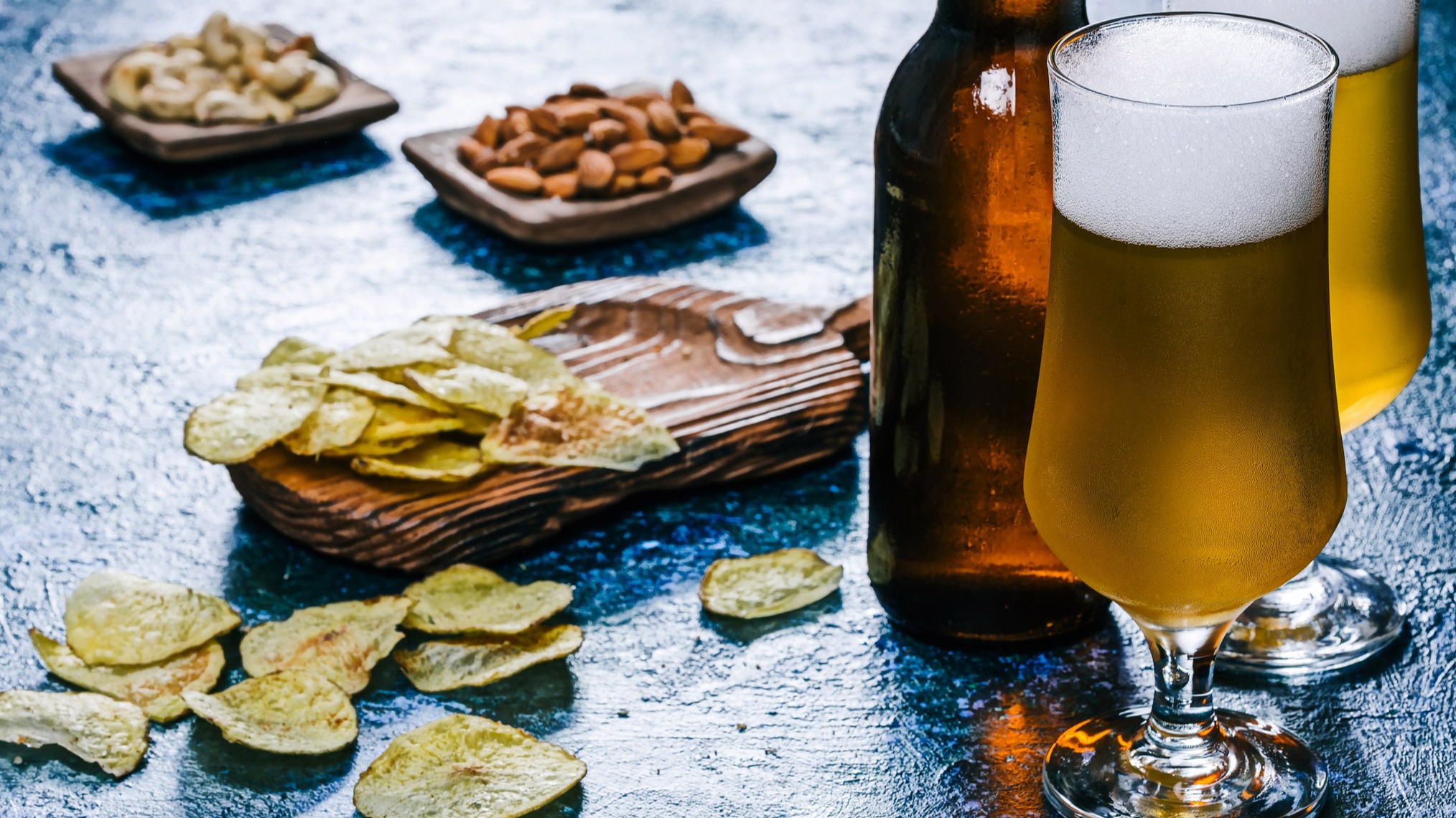 Pullo ja kaksi lasia vaaleaa olutta, perunalastuja ja pähkinöitä pikku purtavaksi.