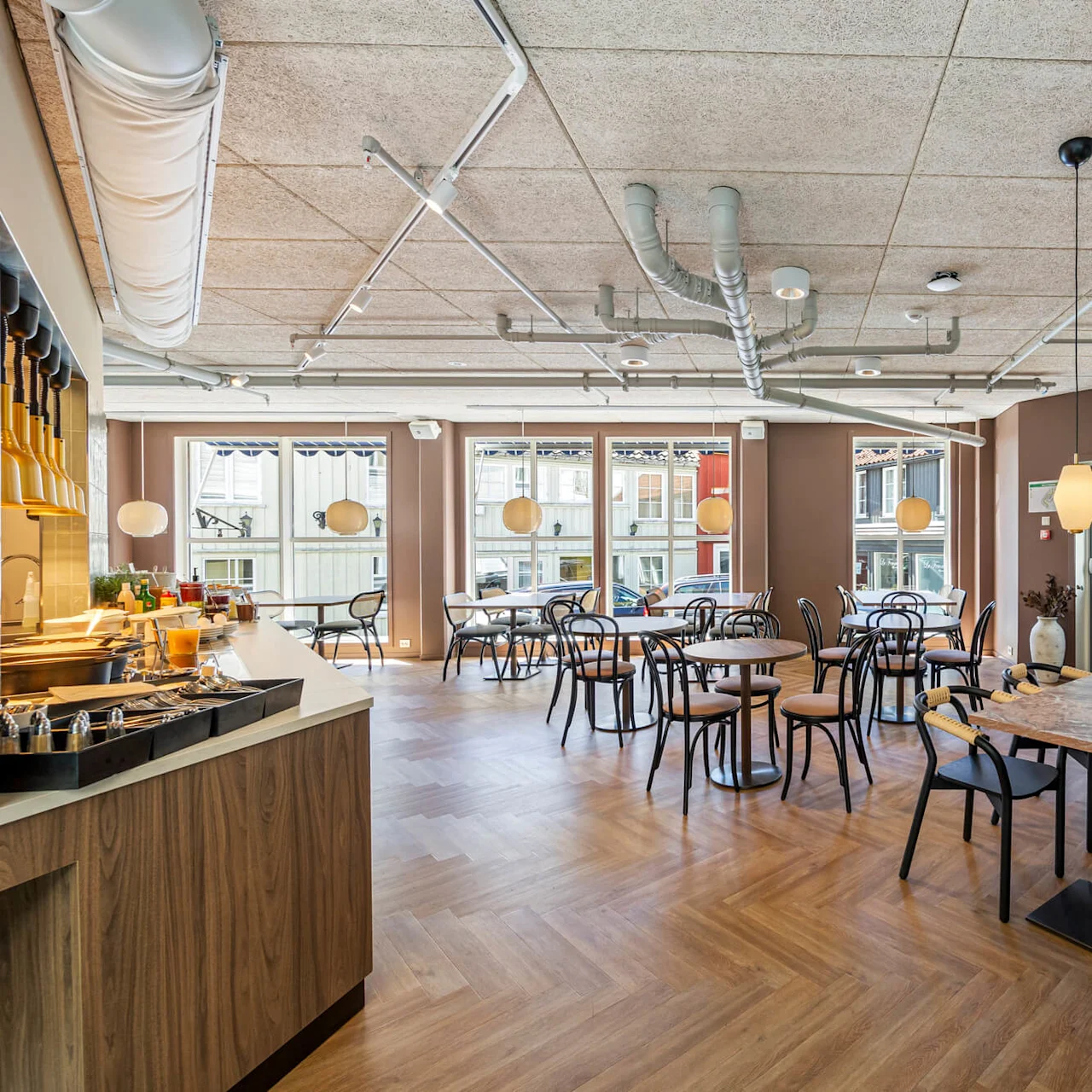 A modern dining area with arranged tables and chairs, bright pendant lights, and exposed ductwork overhead, providing an urban, cozy ambiance.
