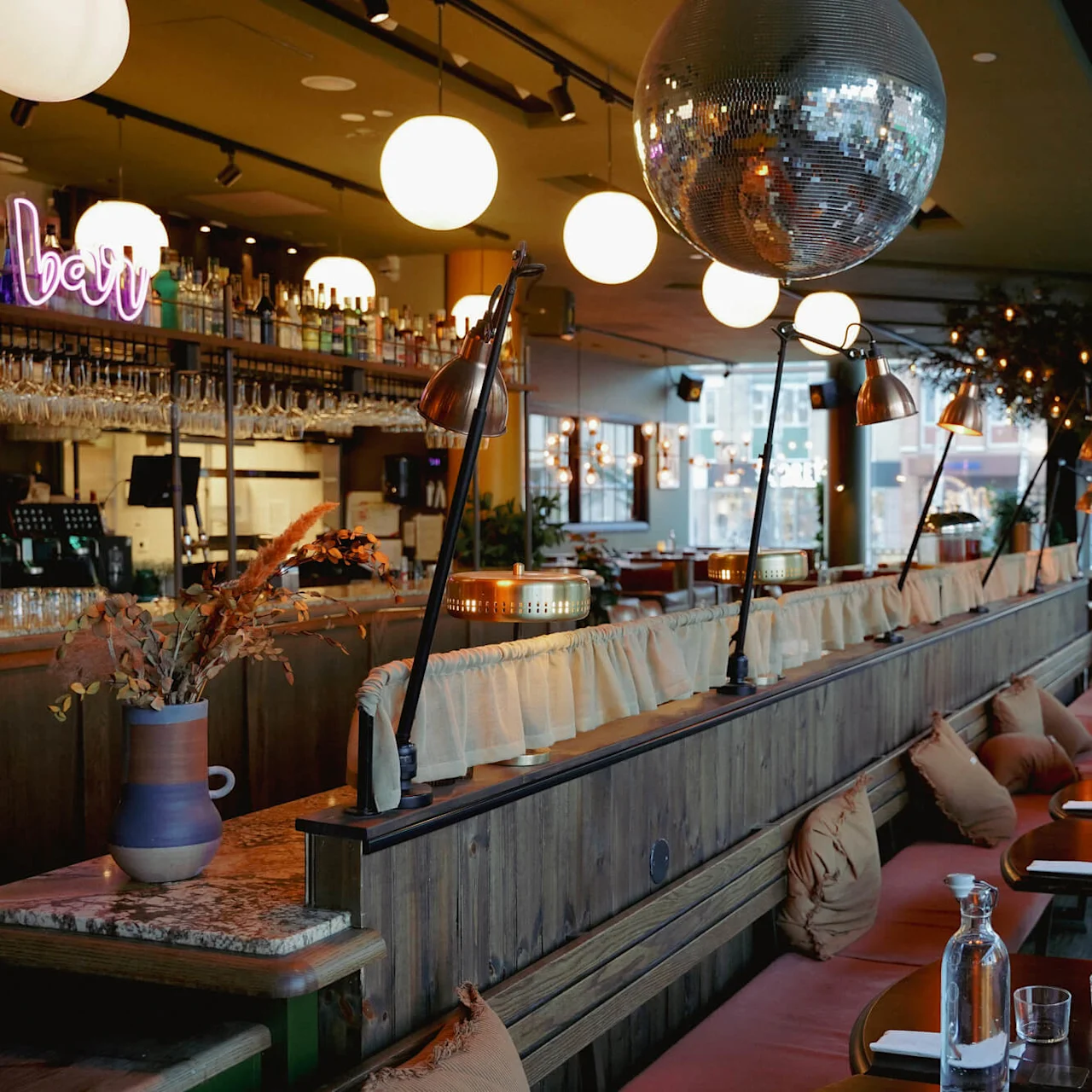 Indre af en hyggelig restaurant med bordpladser, en bardisk og varm belysning, herunder en stor diskokugle.