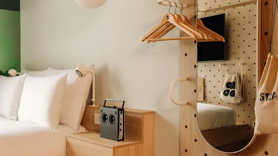 Modern hotel room at Hobo Oslo with a raised bed, radio, and a stylish pegboard wall with a mirror and hangers.