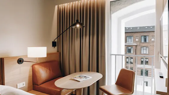 Ett mysigt hotellrum med en säng, ett litet bord och ett fönster med utsikt över en stadsbyggnad.