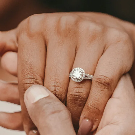 To hender forsiktig flettet sammen, den ene prydet med en glitrende forlovelsesring, symboliserer kjærlighet og engasjement.
