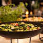 Et nærbilde av en frisk grønn salat med brokkoli, squash og reddiker i en mørk bolle på en buffet.