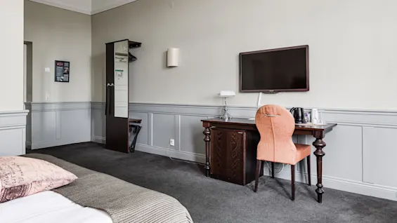 A neat hotel room with a bed, desk, TV, and coffee-making facilities, well-lit and clean.