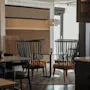 Viihtyisä ravintola, jossa mustat tuolit, pyöreät pöydät ja kuvioitu seinä. Vanha mainos tekstillä 'Otto Hultbe MALA'.