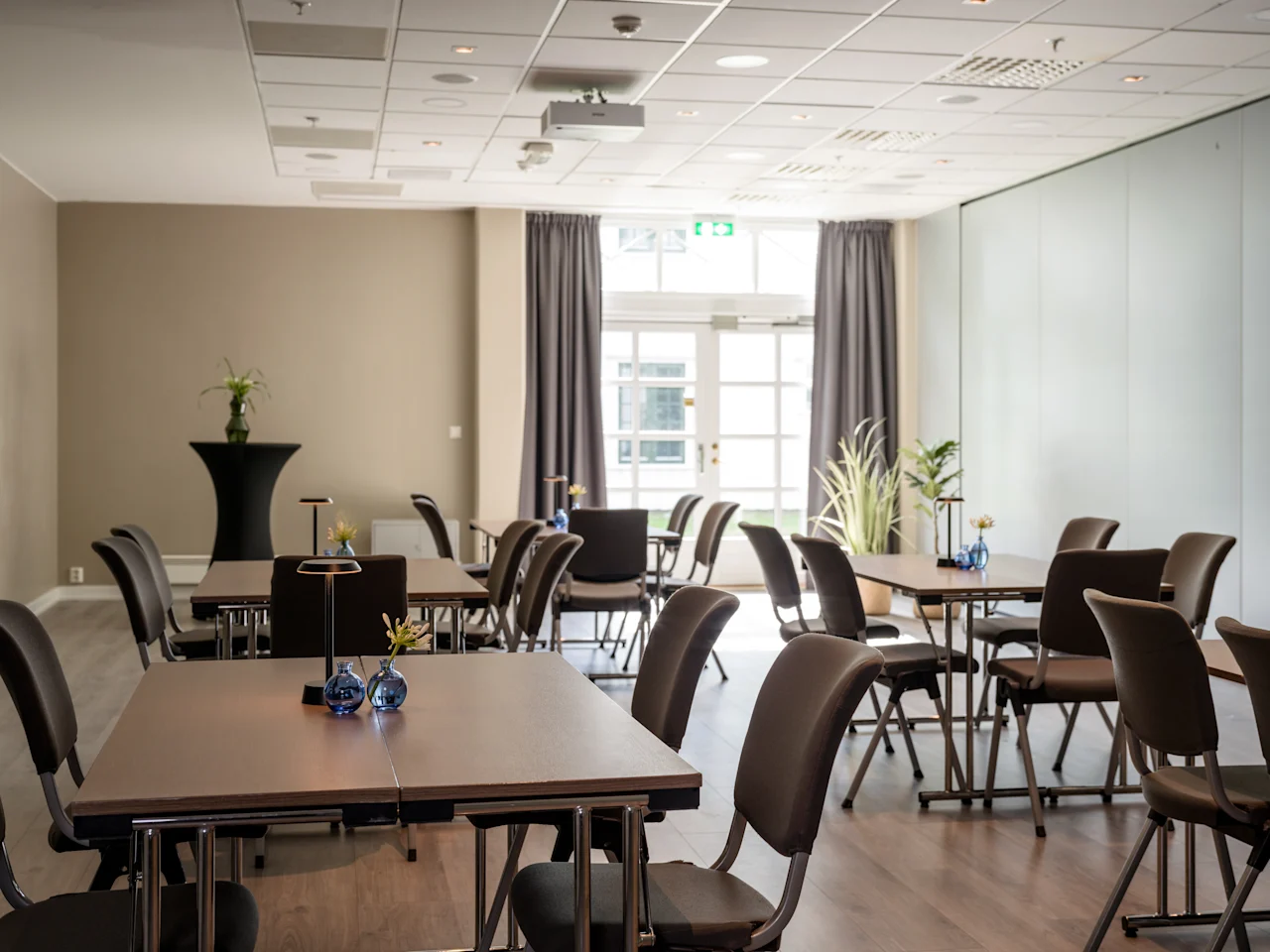 Ett modernt, ljust konferensrum med flera bord och stolar arrangerade för ett möte, med projektor och stora fönster.