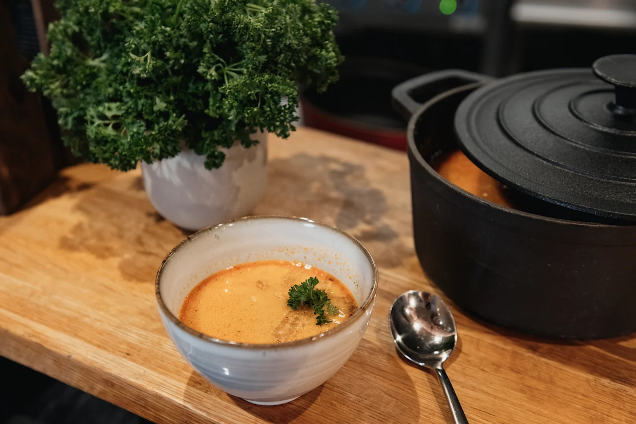 A comforting bowl of soup with a spoon and a cooking pot on a wooden table at Home Hotel Uppsala.