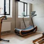 Fitness room at Home Hotel Uppsala with modern wooden exercise equipment including a stationary bike, treadmill, and rowing machine.