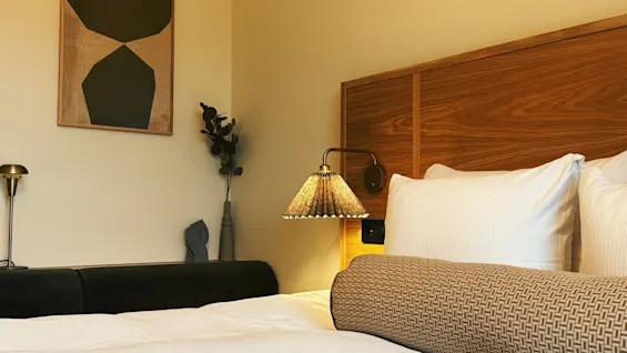 Ett mysigt hotellrum med en bekväm säng, sänggavel i trä och varm belysning från en sänglampa.