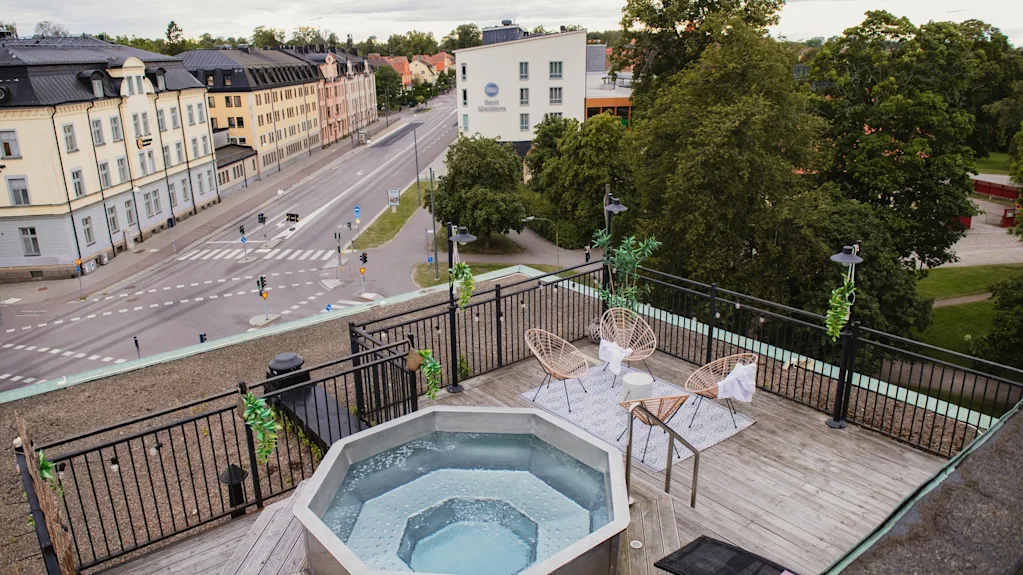 Rooftop terrace with a bubbling hot tub and comfortable seating, overlooking a city street and buildings.