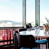 A restaurant with tables and chairs, featuring a large window overlooking an airport control tower.