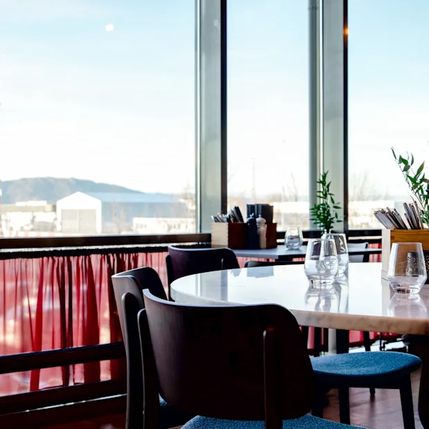 En restaurant med borde og stole, med et stort vindue, der vender ud mod et lufthavnstårn.