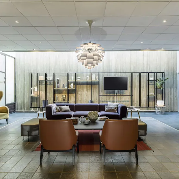 Moderne og koselig hotellobby med stilfulle lenestoler, en mørk sofa og en iøynefallende taklampe.