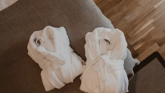 To bløde hvide badekåber pænt foldet, inviterer til et øjebliks afslapning og komfort i hyggelige omgivelser. 🧖‍♀️✨