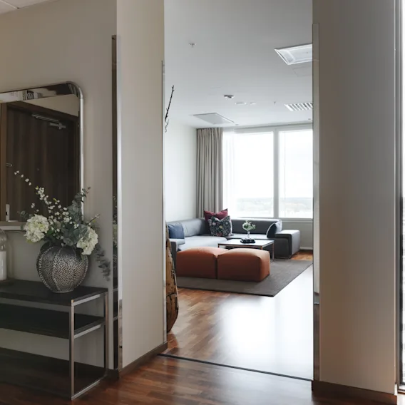 En modern hall med ett dekorativt konsolbord och spegel, som leder in till ett ljust vardagsrum med soffa och stora fönster.