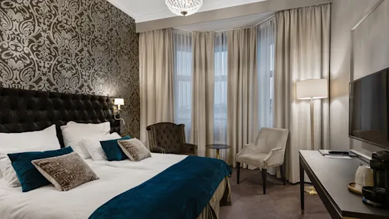Et luksuriøst hotelværelse med en stor seng, elegant tapet, komfortable siddepladser og et skrivebord med TV.