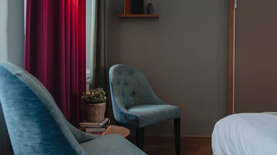 A cozy seating area in a room at Home Hotel Uppsala, featuring two comfortable chairs, a small table with books, and red curtains.