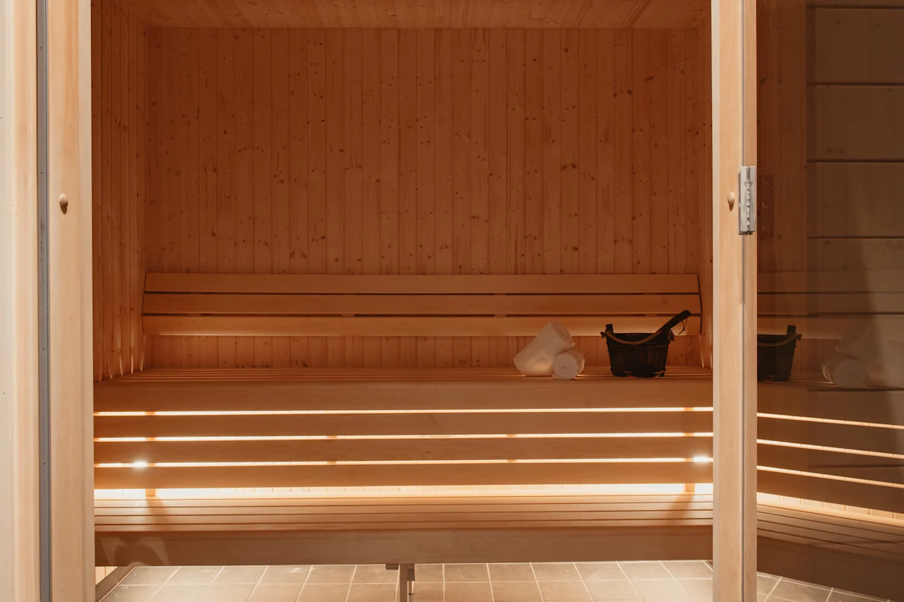 En varm, indbydende træsauna med bænke, en spand og håndklæder, klar til en afslappende oplevelse.