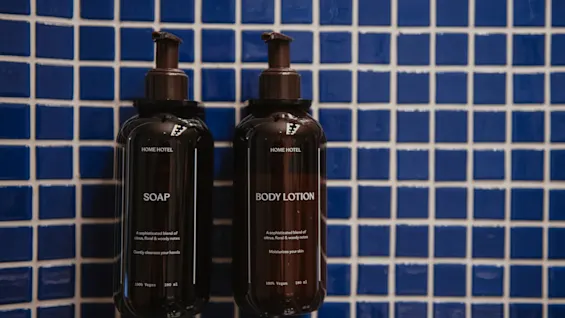 Home Hotel Uppsala provides soap and body lotion in dark bottles on a blue tiled wall. Both are 100 percent vegan with sophisticated notes.