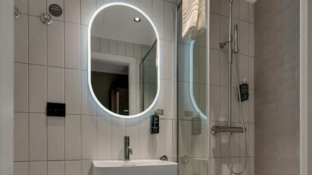 A modern bathroom with LED mirror, sink, towels, toilet, and a glass shower enclosure.