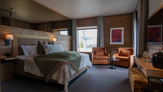 Ett mysigt hotellrum med en stor säng, träväggar och en sittgrupp vid ett fönster med utsikt över naturen.