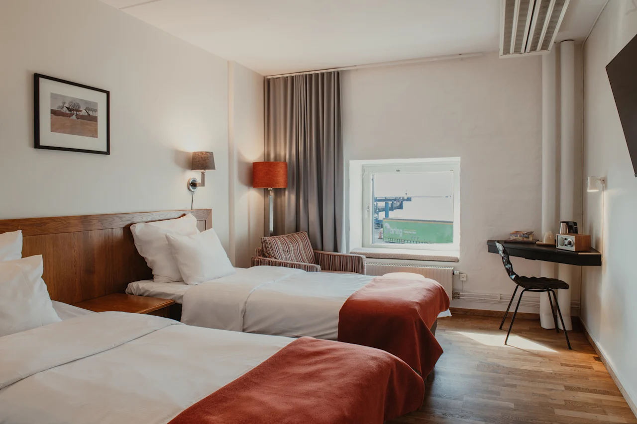 Viihtyisä hotellihuone, jossa kaksi erillistä sänkyä, työpöytä ja ikkuna, josta näkyy teollisuusalue.
