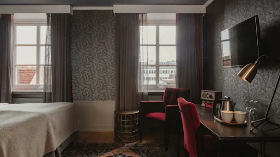 Ett inbjudande hotellrum på Home Hotel Grand, Helsingborg, med en bekväm säng, sittgrupp och ett skrivbord med förfriskningar.