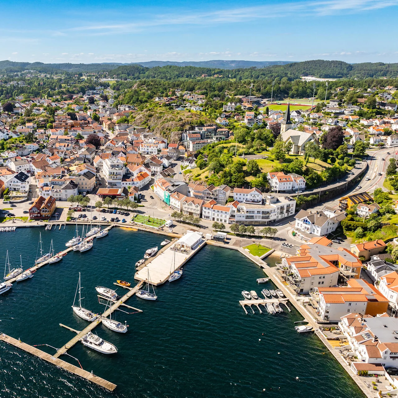 Aerial view of a coastal town with boats docked at piers, surrounded by dense buildings and green hills.