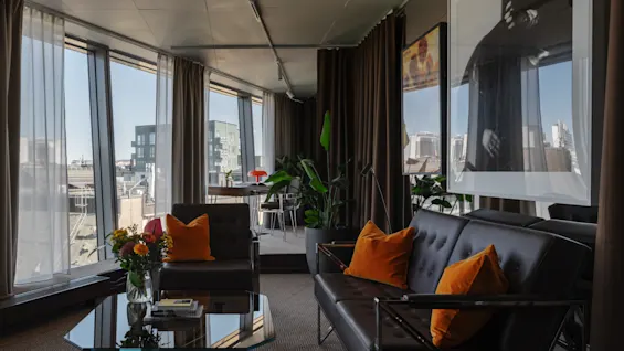 A modern and comfortable lounge area at Clarion Hotel Sign with a sofa, armchair, coffee table, and large windows offering city views.