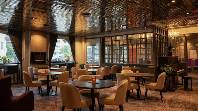 A hotel lounge with a reflective ceiling, comfortable seating, a fireplace, and a piano, offering a warm and inviting space.