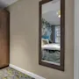 A framed mirror view into a hotel room, with green floral accents in both rooms.