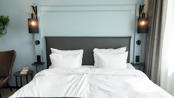 Et koselig hotellrom med en oppredd seng, nattbordslamper og en komfortabel stol.