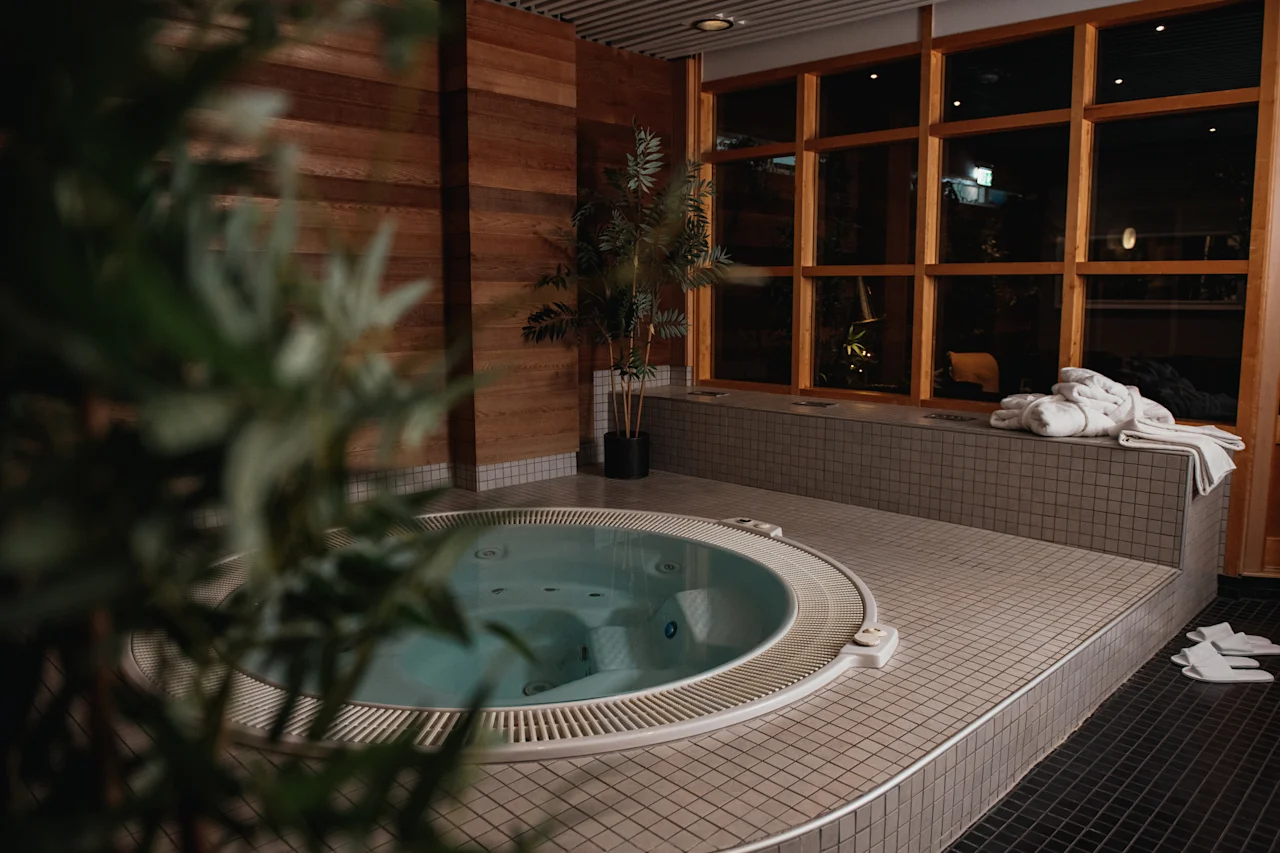 Ett inbjudande inomhusjacuzziområde med varm belysning, stora fönster och fräscha handdukar, perfekt för avkoppling.