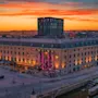 Ett stort hotell i klassisk stil upplyst i rosa och gult under en färgstark solnedgång i staden.