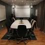 Ett modernt konferensrum med ett stort vitt bord, svarta stolar, whiteboards och en projektorduk, redo för ett möte.