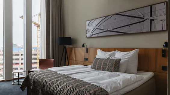 Et moderne hotellrom med en komfortabel seng, stort vindu med utsikt over byen og stilfull innredning.