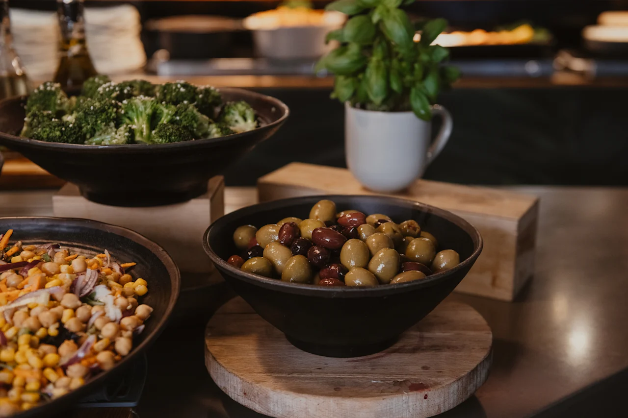 A vibrant buffet spread at Home Hotel Uppsala featuring fresh broccoli, a colorful chickpea salad, and a bowl of mixed olives.