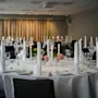 A beautifully set banquet hall with round tables, white tablecloths, candles, and floral centerpieces, ready for guests.