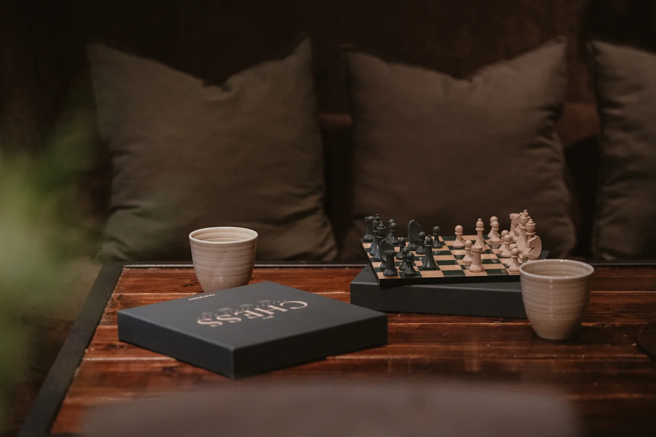 Viihtyisä näkymä shakkipelillä, kahdella keraamisella kupilla ja mustalla CHESS-laatikolla puupöydällä, valmiina peliin.