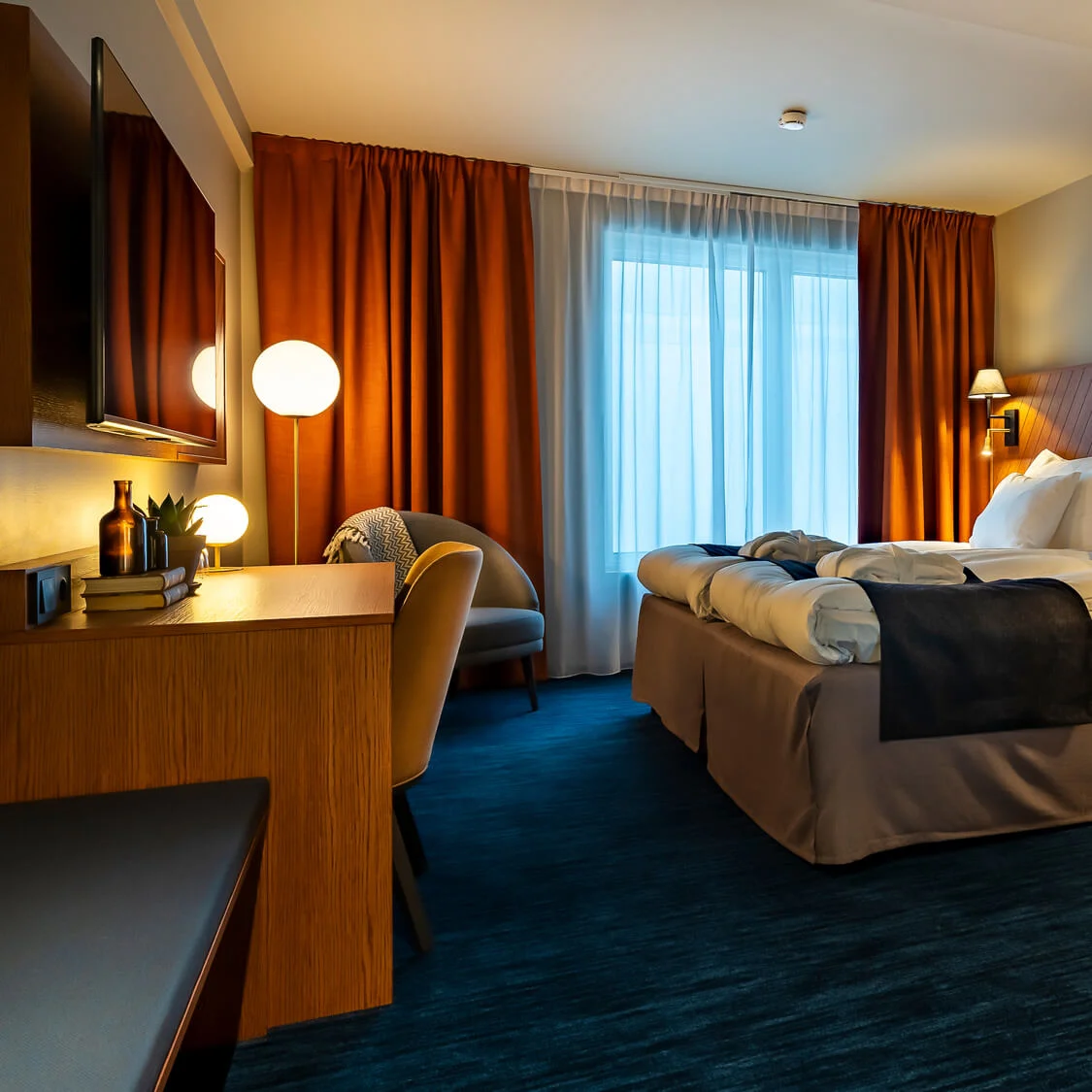 Ett välupplyst hotellrum med en stor säng, möblering och varma färgaccent.