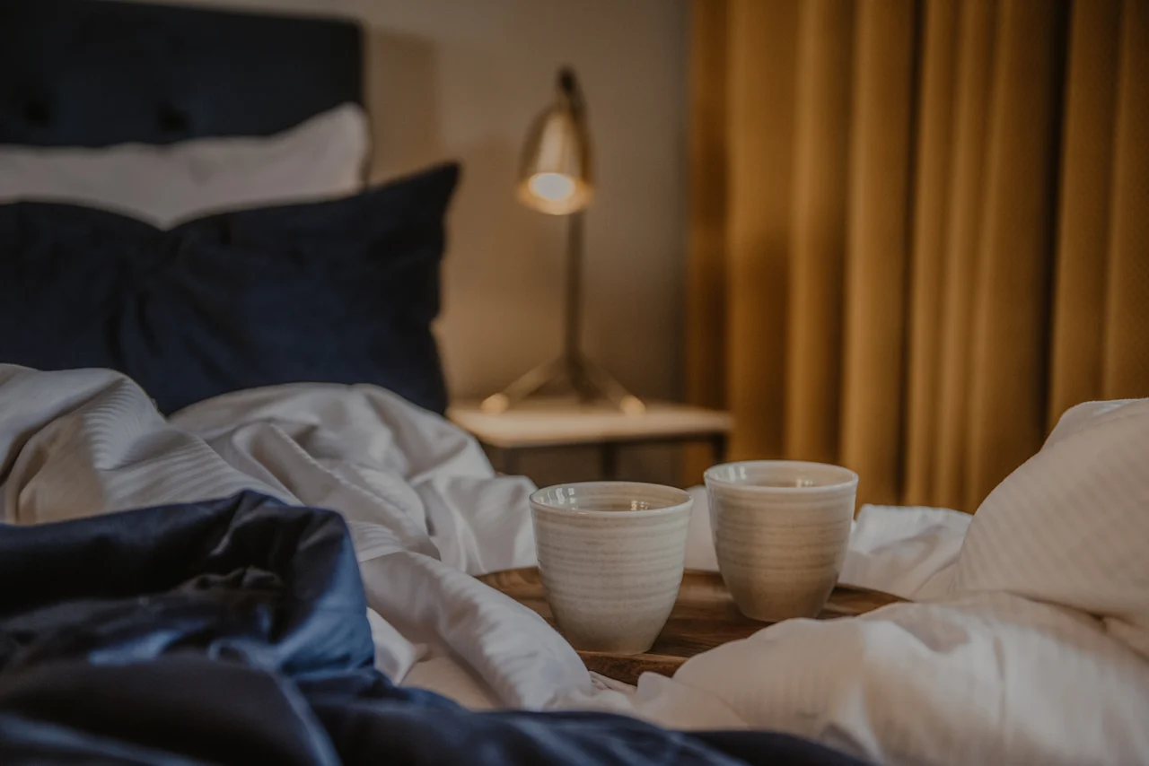 En mysig hotellsäng med två koppar på en bricka, redo för en avkopplande stund på Home Hotel Grand, Helsingborg.