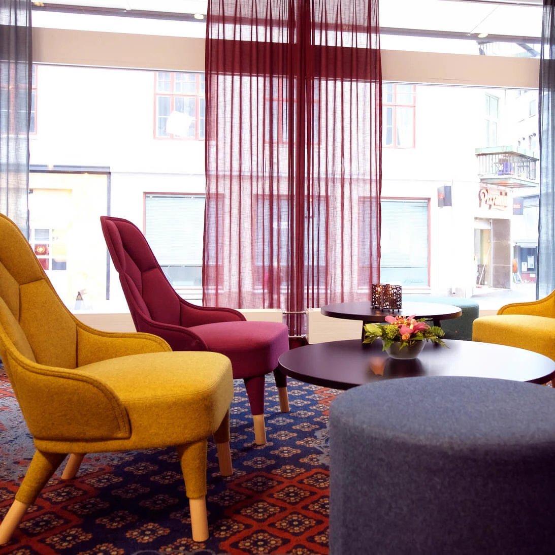 Fargerike lenestoler arrangert i en lys lounge med store vinduer og dekorative gardiner, sentrert rundt et svart kaffebord.