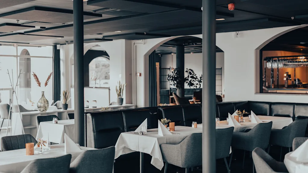 En modern restaurangmiljö med dukade bord, vita dukar och eleganta mörka stolar.