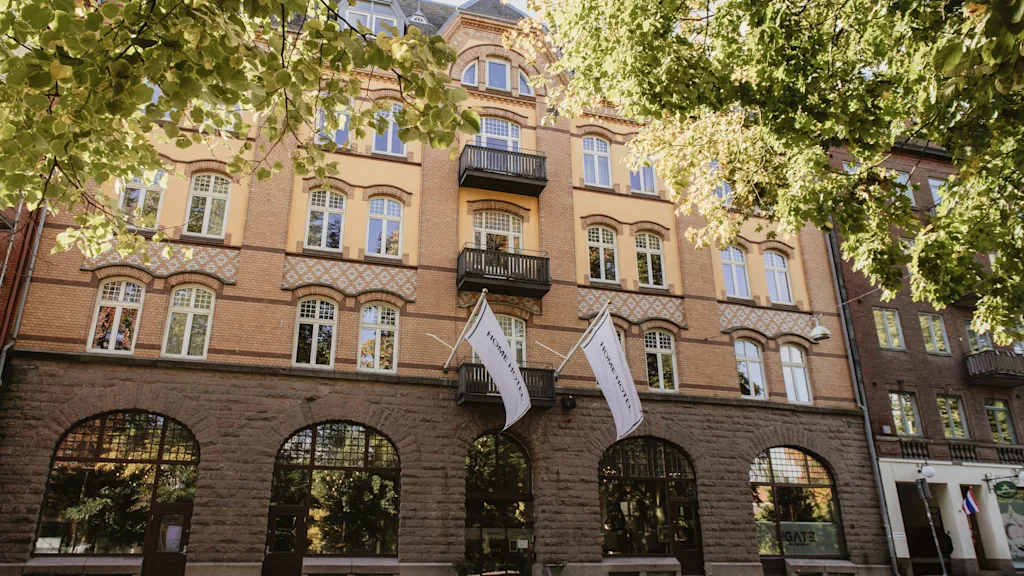 Home Hotel Norre Park in Halmstad, a charming building with flags, framed by green trees on a sunny day.