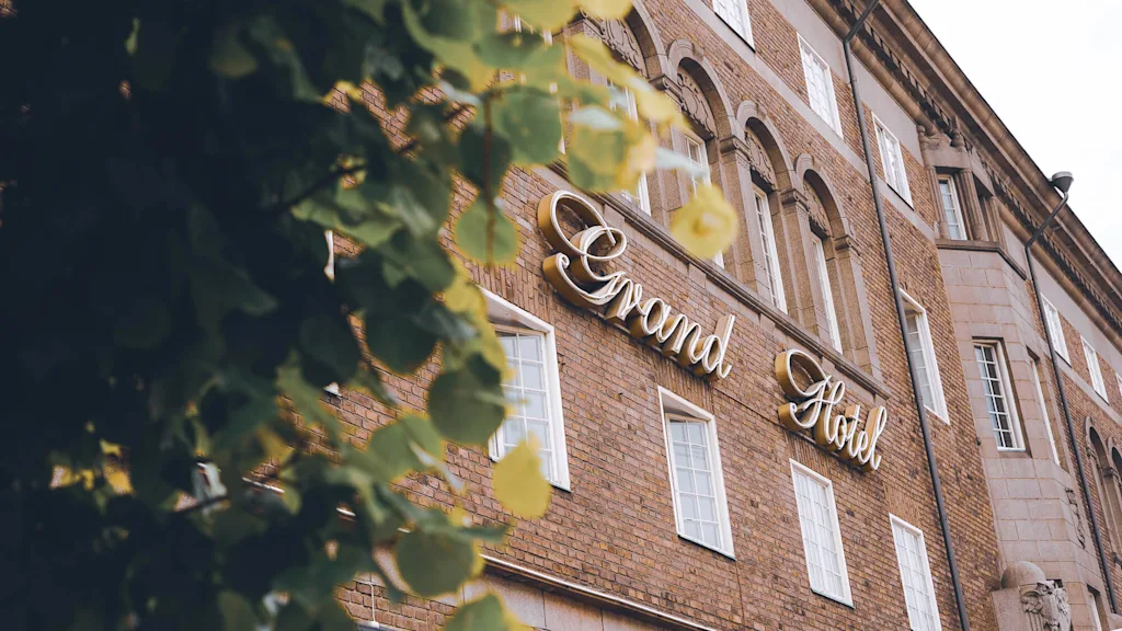 En murstensbygning med skiltet "Grand Hotel", indrammet af slørede blade.